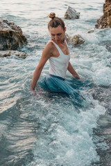 Pretty woman posing in the sea waves in evening. Fashion photoshoot in nature.
