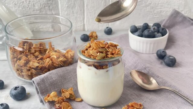 Yogurt with muesly granola and blueberries. Spoon with granola filling the jar.