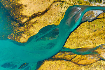 A drone view of the river on the field. An aerial view of an autumn landscape. Winding river among the meadows. Turquoise mountain water. Landscape with soft light before sunset.
