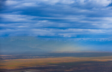 An autumn fall view on Alazani valley in Kakheti region, Georgia. Caucasus mountains in the background. Dramatic sky. Clouds.