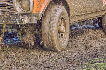 Off road car on a bad road. Expedition in a four-wheel drive orange car to the village on a mountain road. Splashes of mud and water during racing. The wheel is slipping.