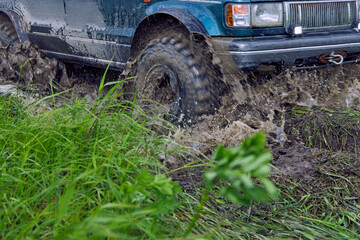 Fototapeta premium The blue SUV is driving on a bad road, interfering with mud and slush with the wheels. Offroader participates in an off-road race.