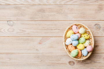 Colorful Easter eggs in wicker basket against colored background, closeup. top view with copy space