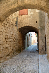 Obraz premium ancient medieval street with narrow entrance, arch and pebbled pathway