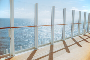 Glass balcony on a luxury cruise ship overlooking the calm blue sea shimmering in sunshine.