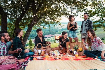 Group of happy friends having fun at the picnic barbecue in a countryside area, celebrating, eating grilled food and drinking tasty wine - obrazy, fototapety, plakaty