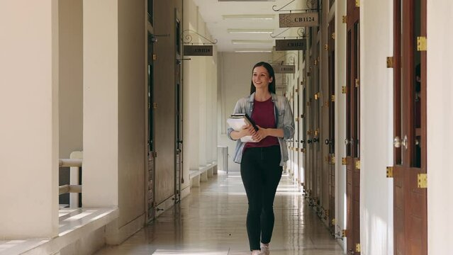 A female college student with a textbook walking along the corridor in the college building. Education, back to school concept.