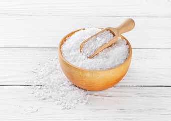Sea salt in wooden bowl with scoop on white wooden background