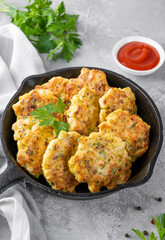 Chicken cutlets made from minced meat, onion, garlic and fresh herbs in a frying pan on a gray concrete background. Top view, selective focus.