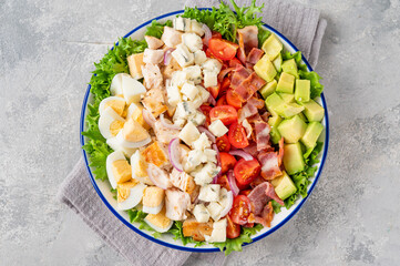 Tradition Cobb salad with fried chicken, avocado, fresh tomatoes, eggs, bacon and cheese on a plate. selective focus