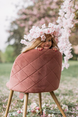 Beautiful and cute baby girl sitting on a stool against the background of a pink sakura flower. Spring. Selective focus photo