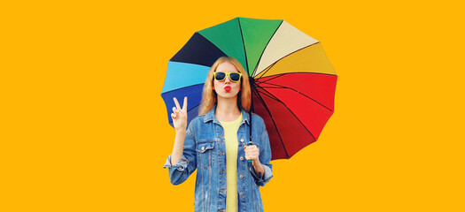 Portrait of beautiful young woman posing with colorful umbrella isolated on yellow background