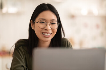 Closeup of happy asian woman using laptop at kitchen