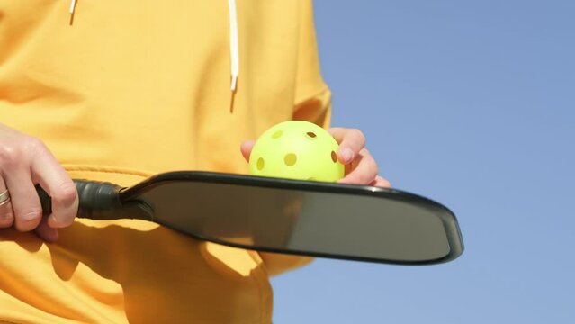 Pickleball paddle and yellow ball close up, woman playing pickleball game, hitting pickleball yellow ball with paddle, outdoor sport leisure activity