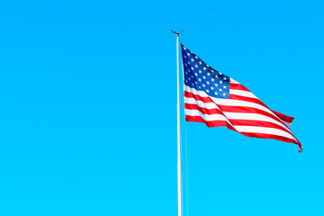 American flag on a tall flagpole flies high against a deep blue sky. Patriotic designs and publications concept.
