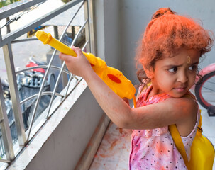 Sweet little Indian girl playing colours on Holi festival, holding pichakaree full of colours, Holi...