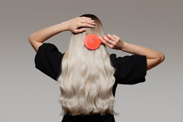 A blonde woman combs her gorgeous hair on a gray background. Back view.