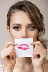 A beautiful woman holds the imprint of her kiss on paper near her face.