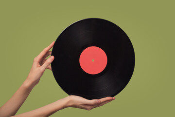 Women's hands hold a vinyl disc. Green background.