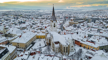 Birds eye view over historic city center of Sibiu, Romania at sunset. Drone photography from above containing the Evangelical Cathedral and Hued square, small square and the big square. 