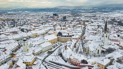 Birds eye view over historic city center of Sibiu, Romania at sunset. Drone photography from above containing the Evangelical Cathedral and Hued square, small square and the big square. 