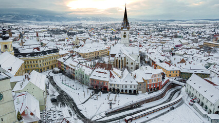 Birds eye view over historic city center of Sibiu, Romania at sunset. Drone photography from above containing the Evangelical Cathedral and Hued square, small square and the big square.  - obrazy, fototapety, plakaty