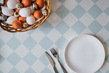 top view, close-up of a spring still life, a background with a place for your text, in the lower right corner an empty white plate with cutlery, in the upper left corner a wicker plate with eggs