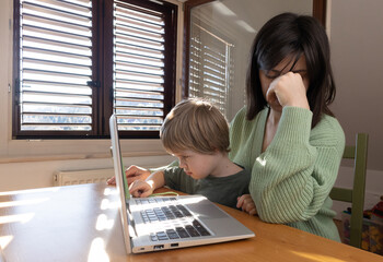 Boy near mom, mom works from home with laptop
