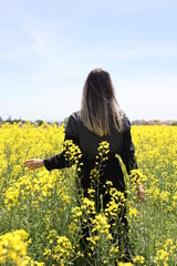 Fototapeta premium Back View of a Young Woman Standing on the Flower Field. Canola Field.