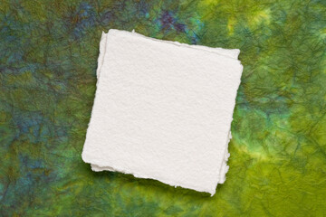 small square sheet of blank white Khadi paper against colorful marbled paper