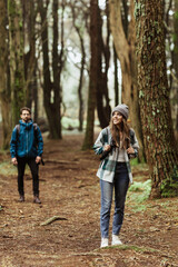 Happy millennial caucasian man and woman in jackets and backpacks travel in cold forest, enjoy adventure