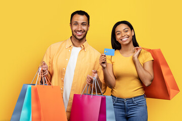 Happy young african american family shopaholics hold many packages of purchases, show credit card
