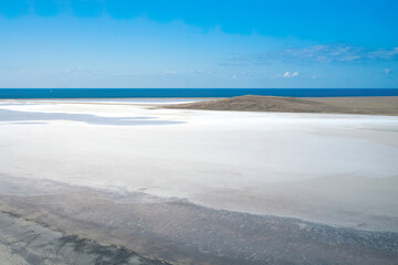 Panoramic view of the white salt lake. In the background is a narrow strip of blue sea merging with the sky. Shot from a drone. Copy space.
