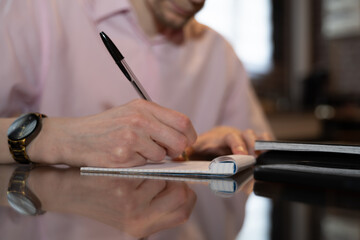 écriture d'une liste sur un bloc note par un jeune homme en chemise rose