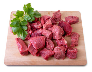 Raw beef diced for stew on wooden cutting board with parsley leaves