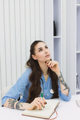 This photo shows a cosmetic dermatologist taking notes at her desk, surrounded by plants, books, and accessories. blue coat and professional focus. thoughtful, serious.