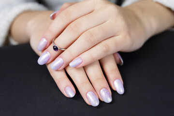 The hands of a young woman. The nails are covered with pearl gel polish with glitter