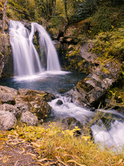 Fototapeta premium Vista de la Cascada de Narahío, con agua cayendo formando un lago azul rodeado de vegetación, en La Coruña, Galicia, verano de 2021.