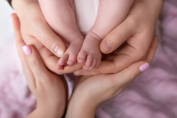 Obraz na płótnie Canvas Little feet of a newborn baby girl in the hands of father and mother on a pink background. baby feet in parental hands