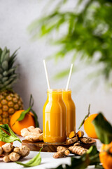 Fresh raw ingredients for detox ginger and turmeric smoothies and already blended mix in a bottles for individual consumption are on the kitchen table surface.