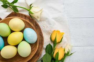 Happy Easter. Easter eggs on rustic table with white and yellow roses. Natural dyed colorful eggs in wooden plate and spring flowers in rustic room.  Toned image. Easter background with copy space.