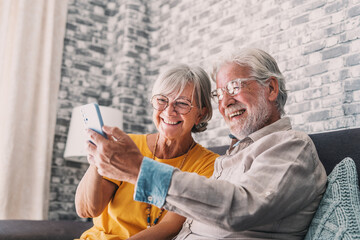Happy retired family couple using mobile phone for video call together, talking to relations, getting good news, having fun, smiling and laughing. Carefree mature pensioners chatting online on cell.