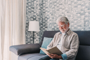 Headshot portrait close up of old happy and relaxed man sitting reading a book at home. Mature male person enjoying free time having fun indoor..