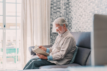 Headshot portrait close up of old happy and relaxed man sitting reading a book at home. Mature male person enjoying free time having fun indoor..