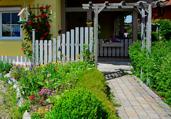 romantyczny kącik wypoczynkowy w ogrodzie, czerwone róże na ścianie domu, wiejski ogród, biały drewniany płot, romantic relaxation corner in garden, cottage garden, white wooden picket fence - obrazy, fototapety, plakaty