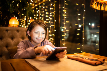 a smiling boy is sitting in a cafe in the evening, talking on the phone, writing sms, waiting for an order in a restaurant.