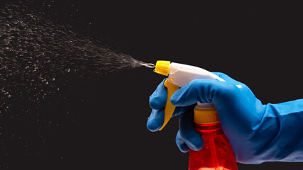 Naklejka premium water sprayer bottle in a hand with gloves on a dark background with liquid spray. household items for home