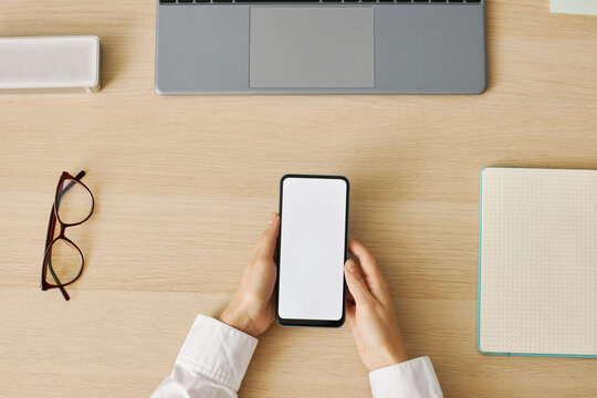Minimal top view woman holding smartphone with white screen mockup at desk