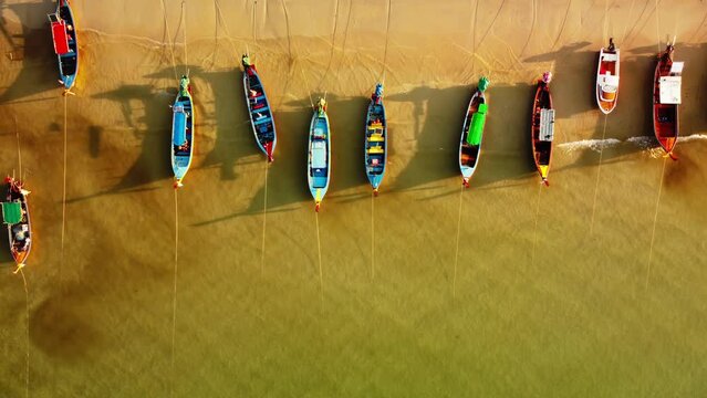 Top view of longtail wooden boats moored in a row on sand beach in warm asian country. Aerial drone landscape of boats on the coast tied with ropes washed by ocean waves. Traditional thai ships