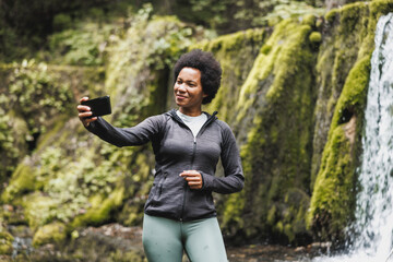 Woman Taking Selfie Near The Waterfall While Hiking On Mountain